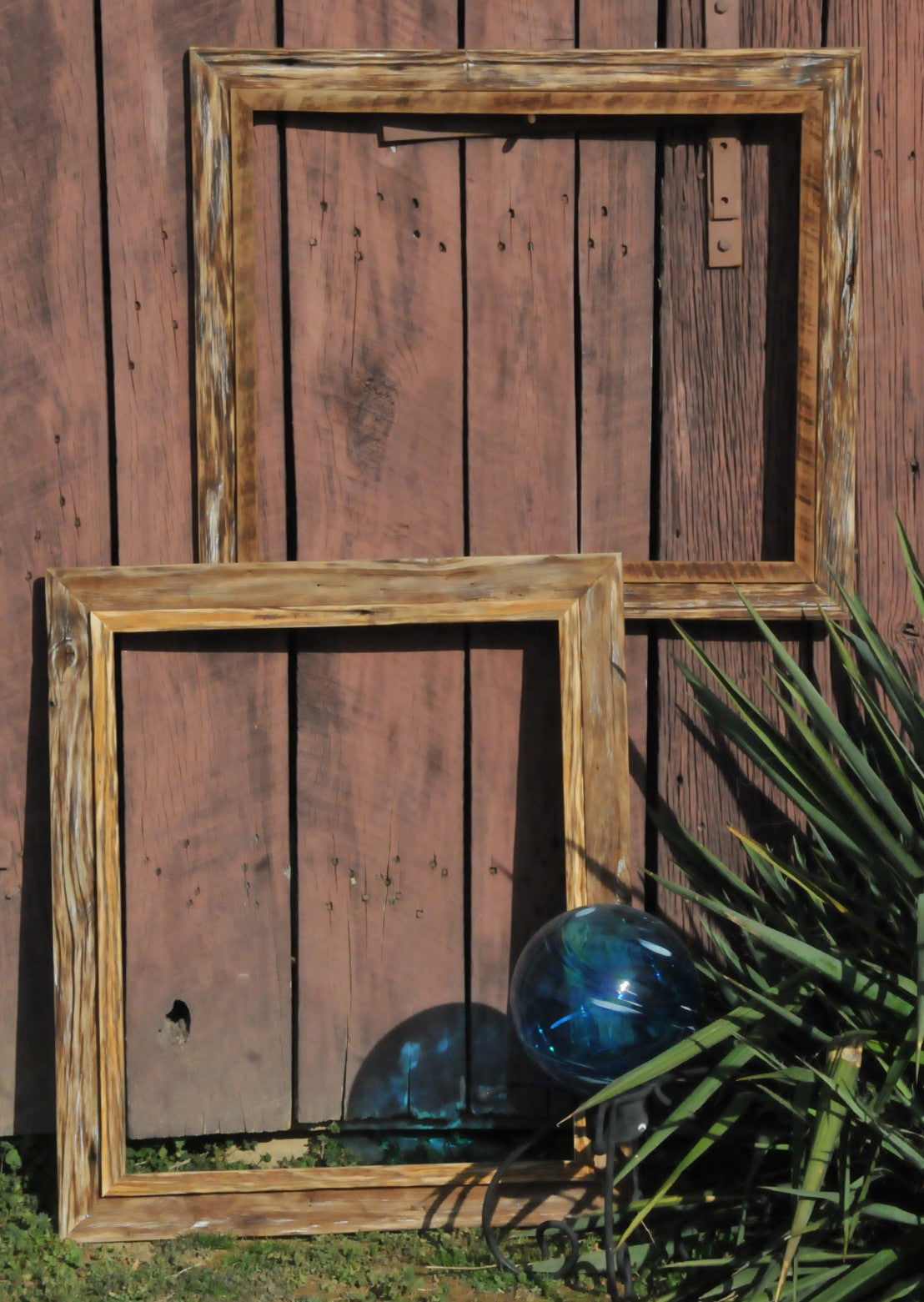 Two samples of Stu Geisbert handcrafted double frames hung from barn exterior wall and adorned with glass blue ball and live cactus